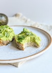 a white plate topped with a piece of bread covered in guacamole