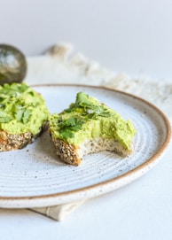 a white plate topped with a piece of bread covered in guacamole
