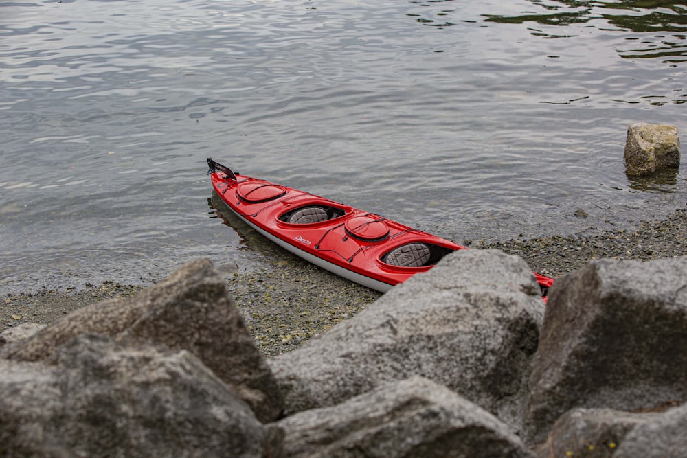 a red kayak sitting on the shore of a lake