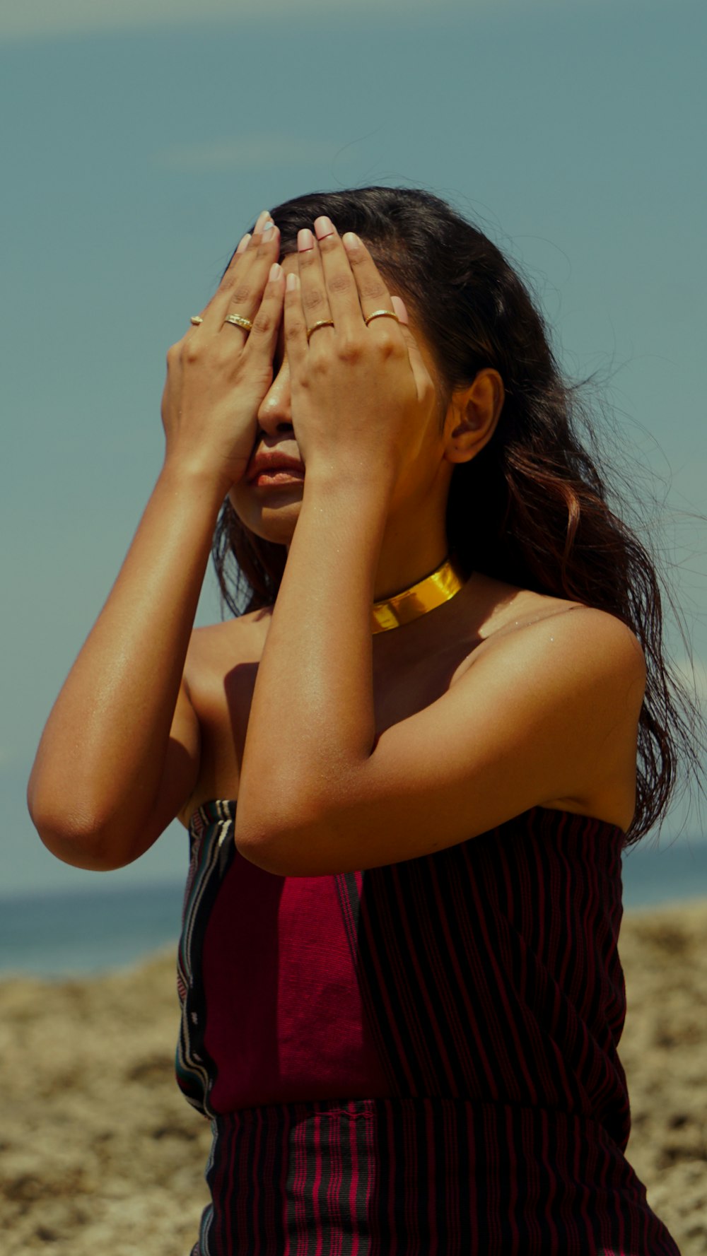 woman in black and red stripe shirt covering her face with her hands