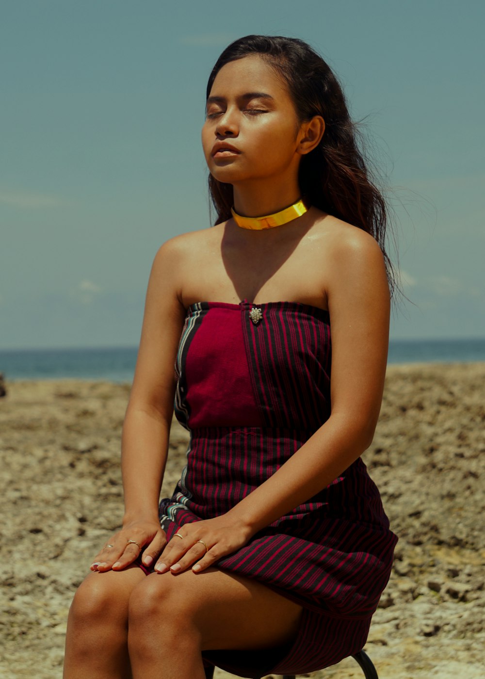 woman in purple and black stripe spaghetti strap dress sitting on brown sand during daytime