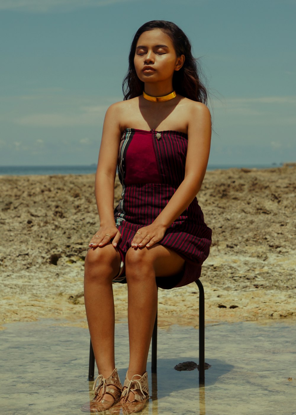 woman in black and red sleeveless dress sitting on chair on beach during daytime