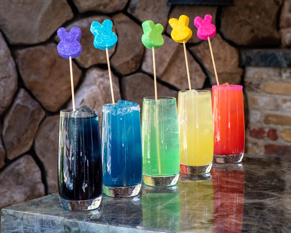 five clear glass jars with blue orange yellow and red liquid