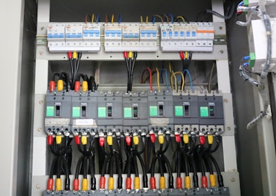 A detailed view of an electrical panel displaying a neatly arranged set of circuit breakers and wiring. The panel includes multiple switches, each labeled with specific codes, and wires of various colors connecting to them. The setup is orderly, with cables aligned and organized through plastic holders.