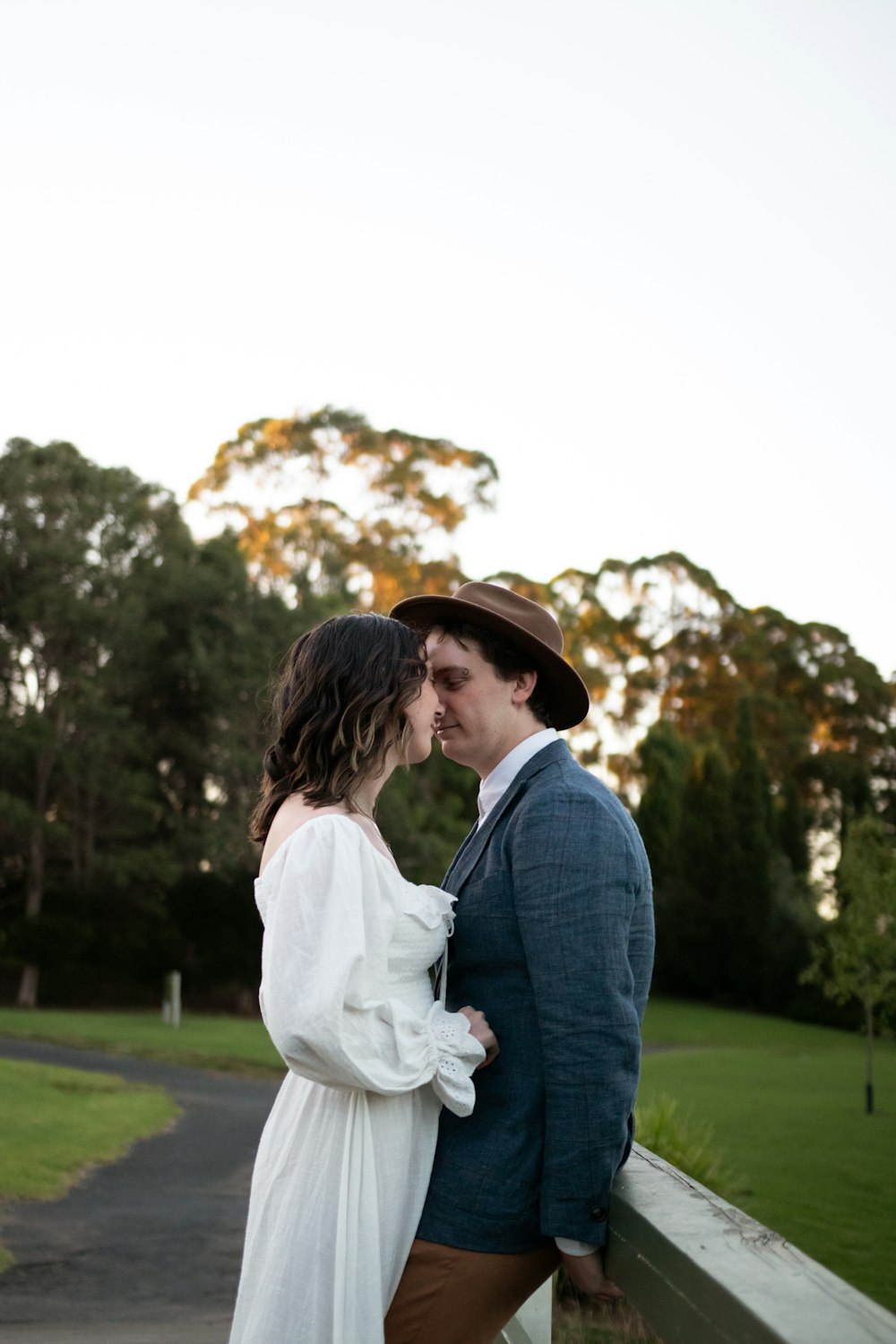 man in blue denim jacket kissing woman in white dress during daytime