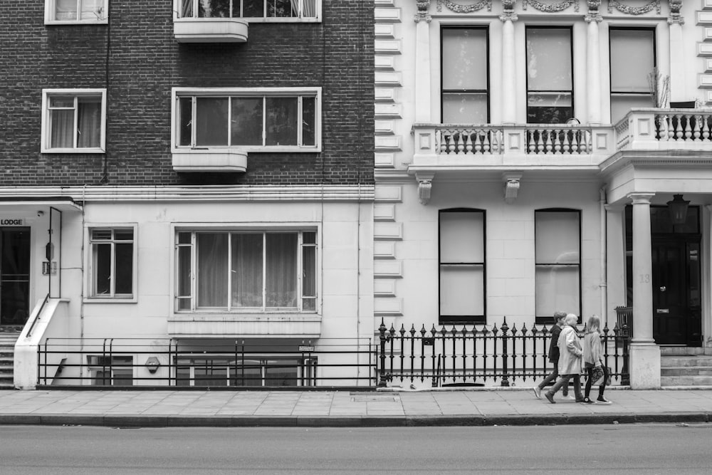 grayscale photo of 2 person sitting on bench in front of building