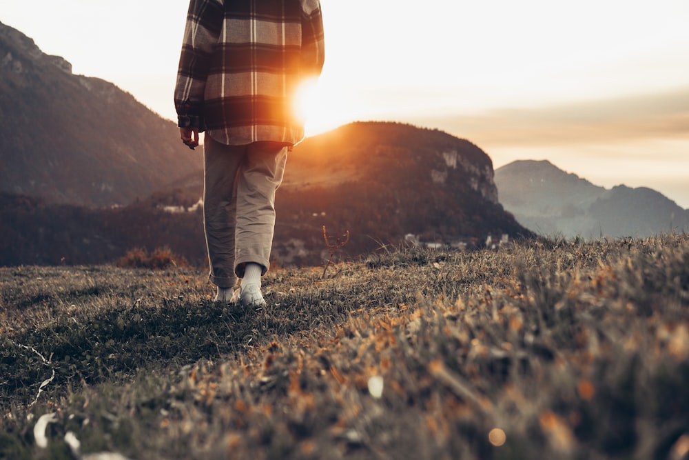 uomo in pantaloni marroni in piedi sull'erba verde durante il tramonto