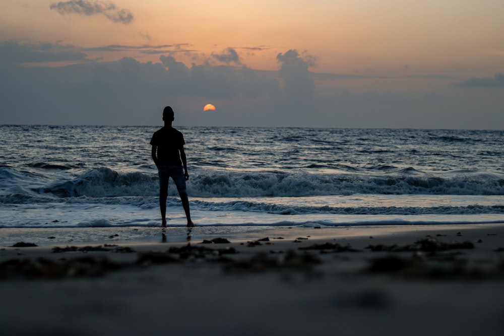 silhouette of man standing on beach during sunset