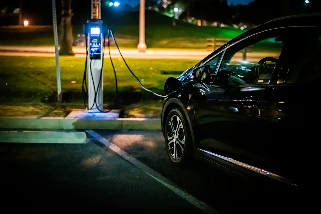 An electric vehicle charging at a lit roadside charger after dark