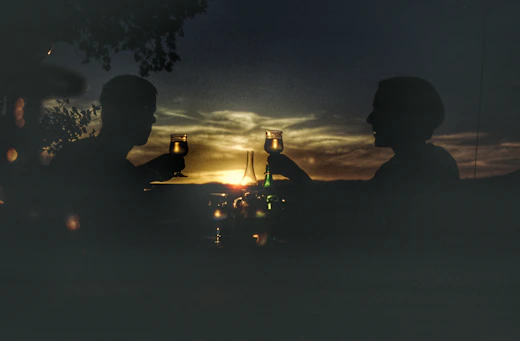 silhouette of two people sitting on ground with lighted candles during night time
