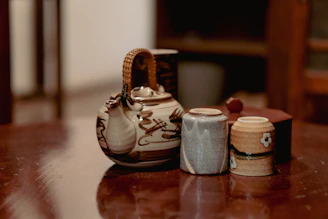 Close-up of a rustic ceramic teapot with a warm glaze, placed on a linen cloth beside dried flowers.