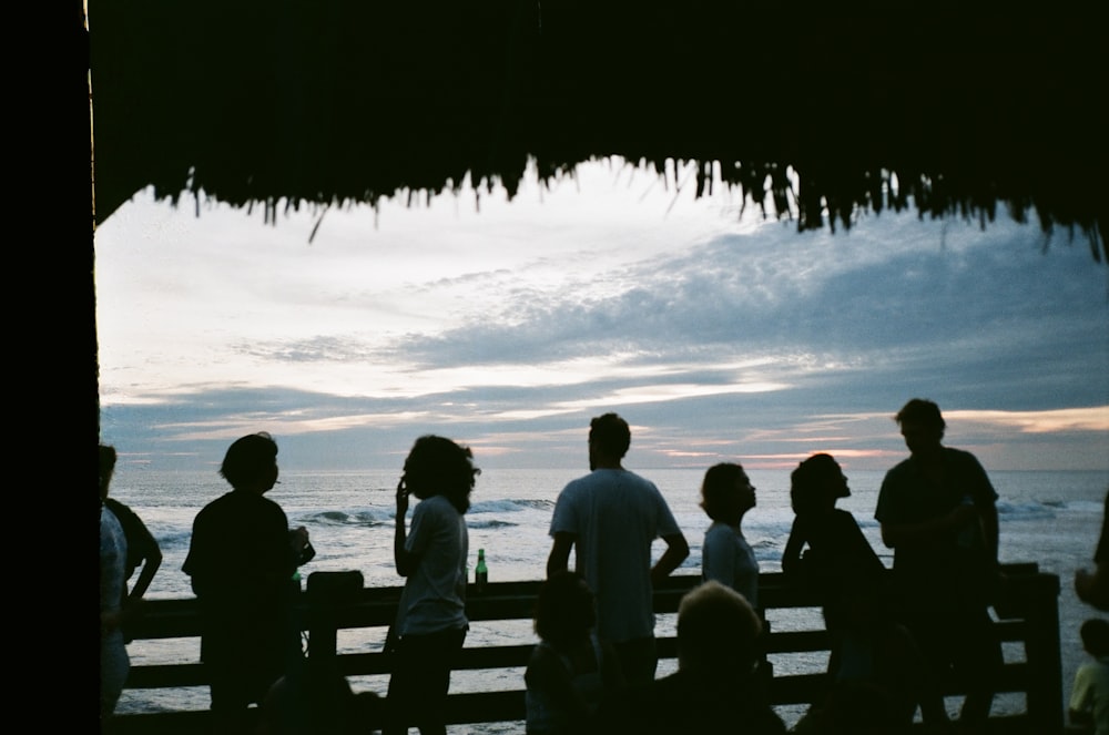 people sitting on wooden bench near sea during sunset