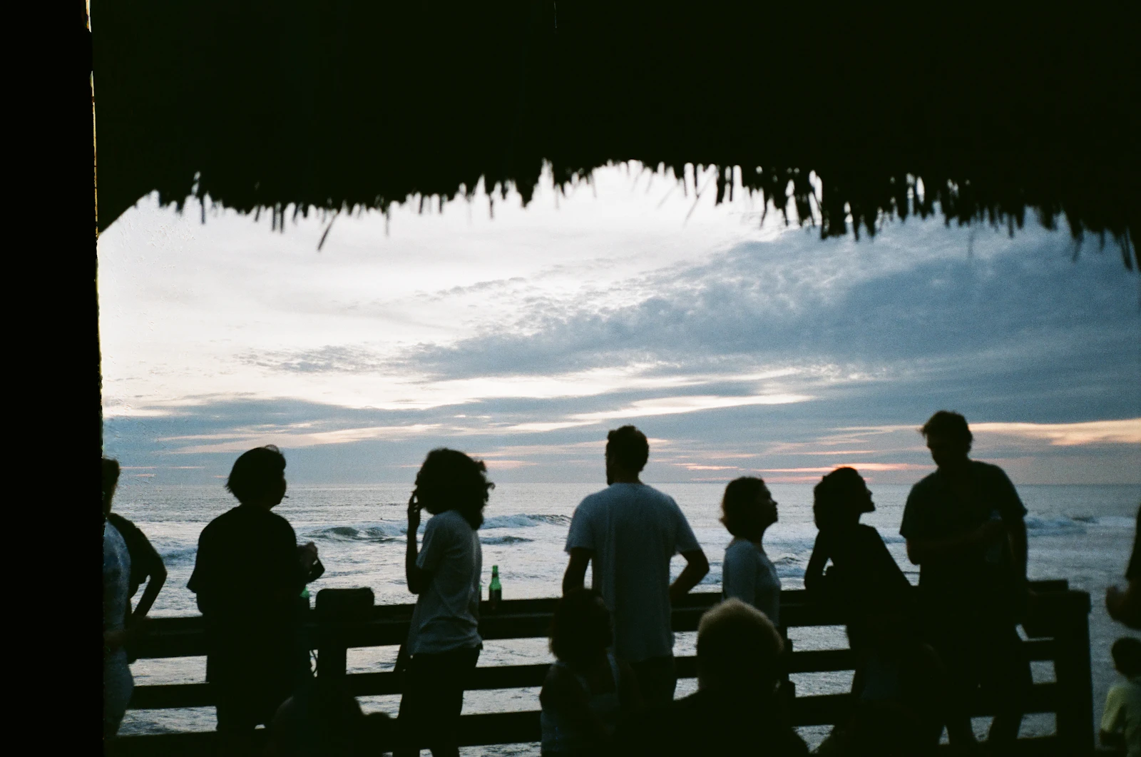People sitting on wooden bench near sea during sunset