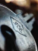 A close-up of a metallic key with engraved details, featuring a prominent logo or text on its surface. The background is blurred, emphasizing the focus on the key's intricate design.