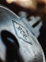 A close-up of a metallic key with engraved details, featuring a prominent logo or text on its surface. The background is blurred, emphasizing the focus on the key's intricate design.