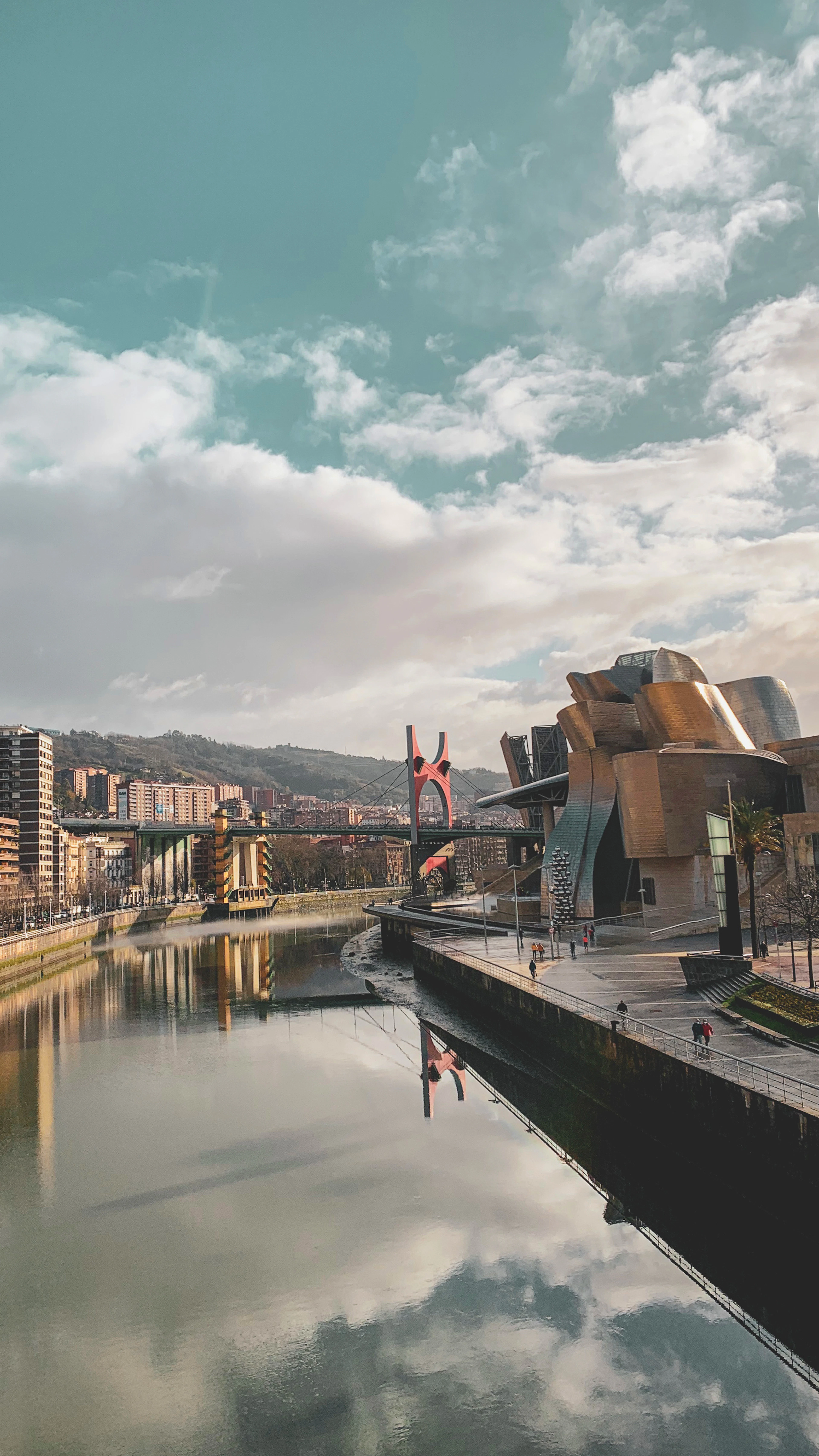 The Nervión curving through Bilbao past the Guggenheim, with the red arch of the La Salve bridge and green hills beyond