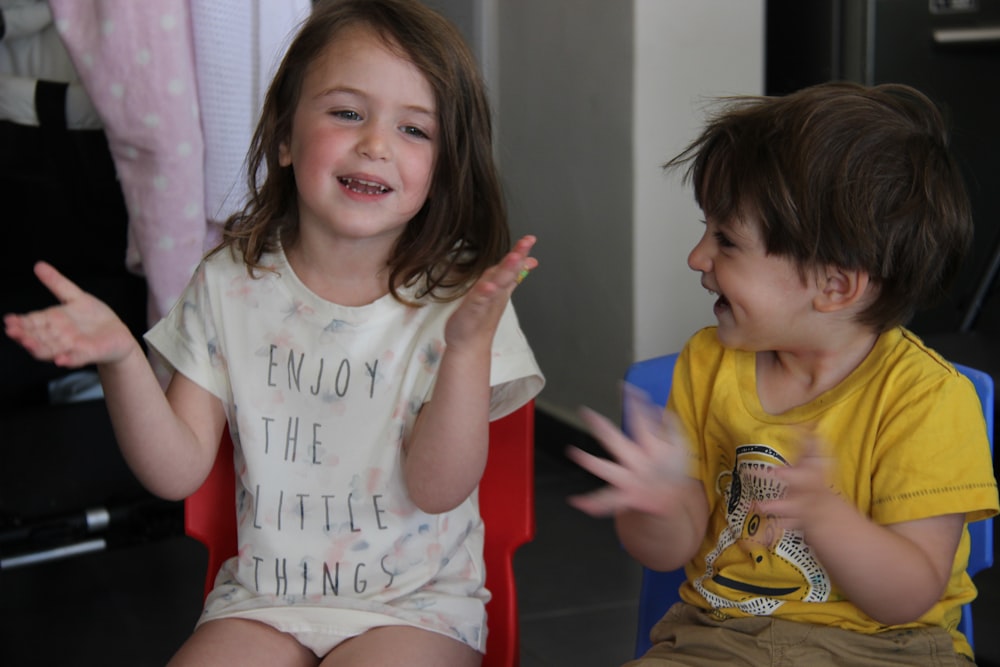 two young children sitting in chairs with their hands in the air