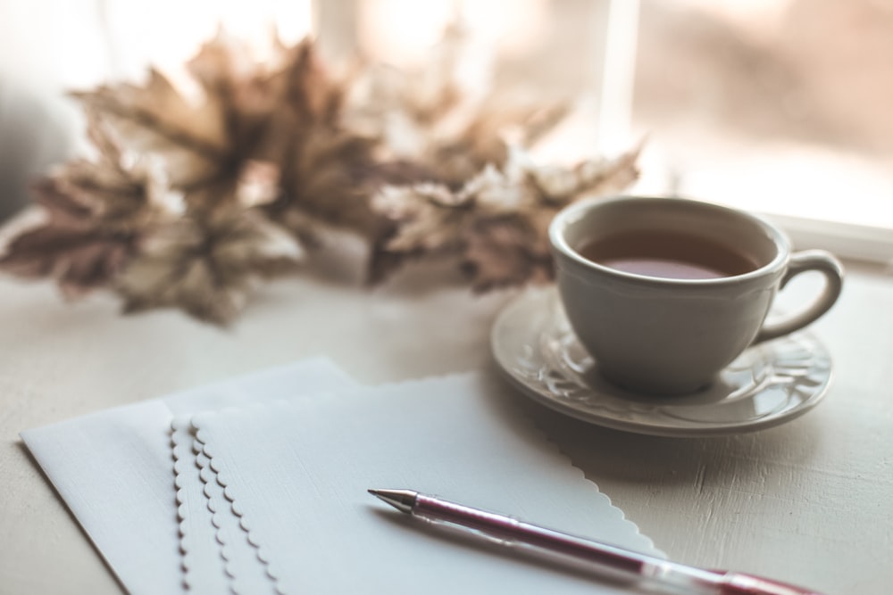 weiße Keramiktasse auf weißer Keramikuntertasse neben rotem Klickstift