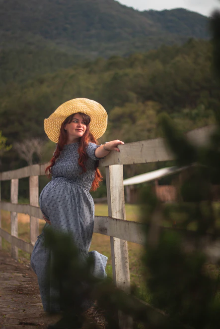 a woman wearing a straw hat leaning on a fence