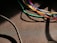 Various colorful cables, including blue, green, yellow, red, and white, are intertwined and cast shadows on a textured dark surface. A thicker black cable moves diagonally across the lower left corner.