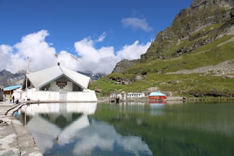 white and brown house near body of water and green mountain under blue sky during daytime
