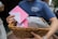 A person holds a wicker basket filled with white and pink envelopes, wearing a blue t-shirt with a logo of a church in New York.