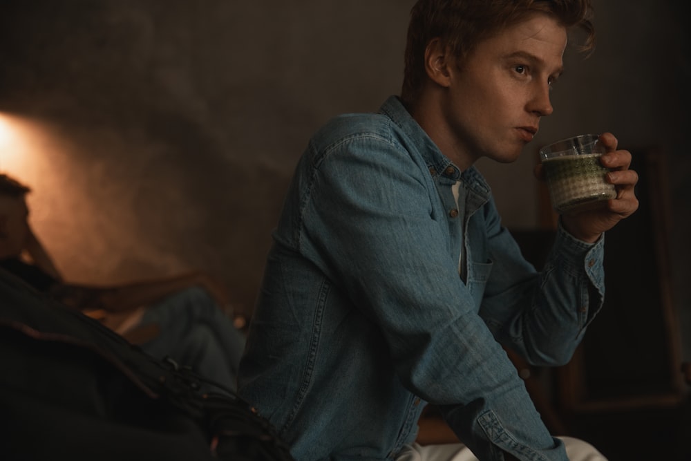 a man sitting on a bed drinking a cup of coffee