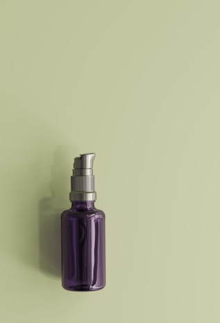A dark purple glass pump bottle with a metallic silver dispenser cap placed against a light green background.