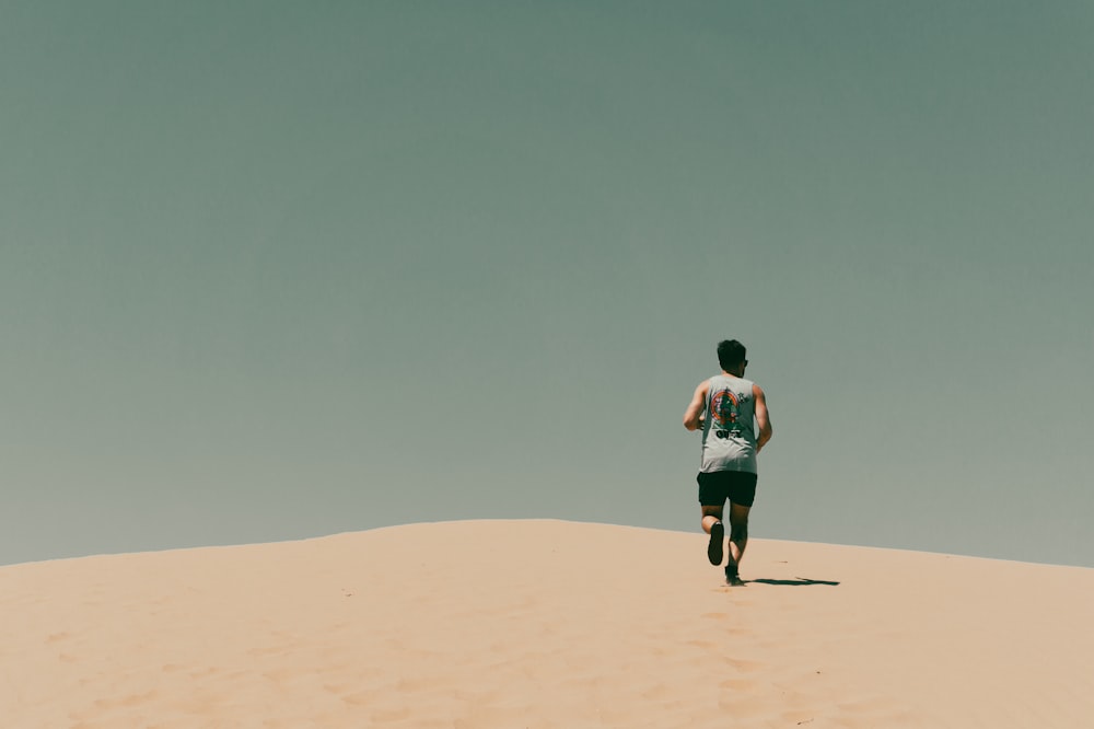 man in blue t-shirt and black shorts walking on brown sand during daytime