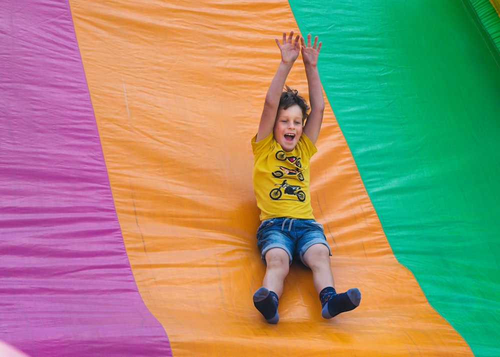 girl in yellow shirt and blue denim shorts lying on orange textile