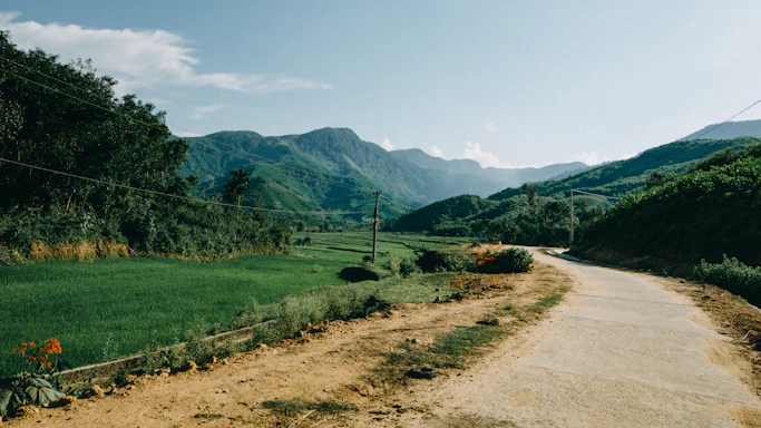 A rural landscape featuring farmland and mountains under a clear blue sky.