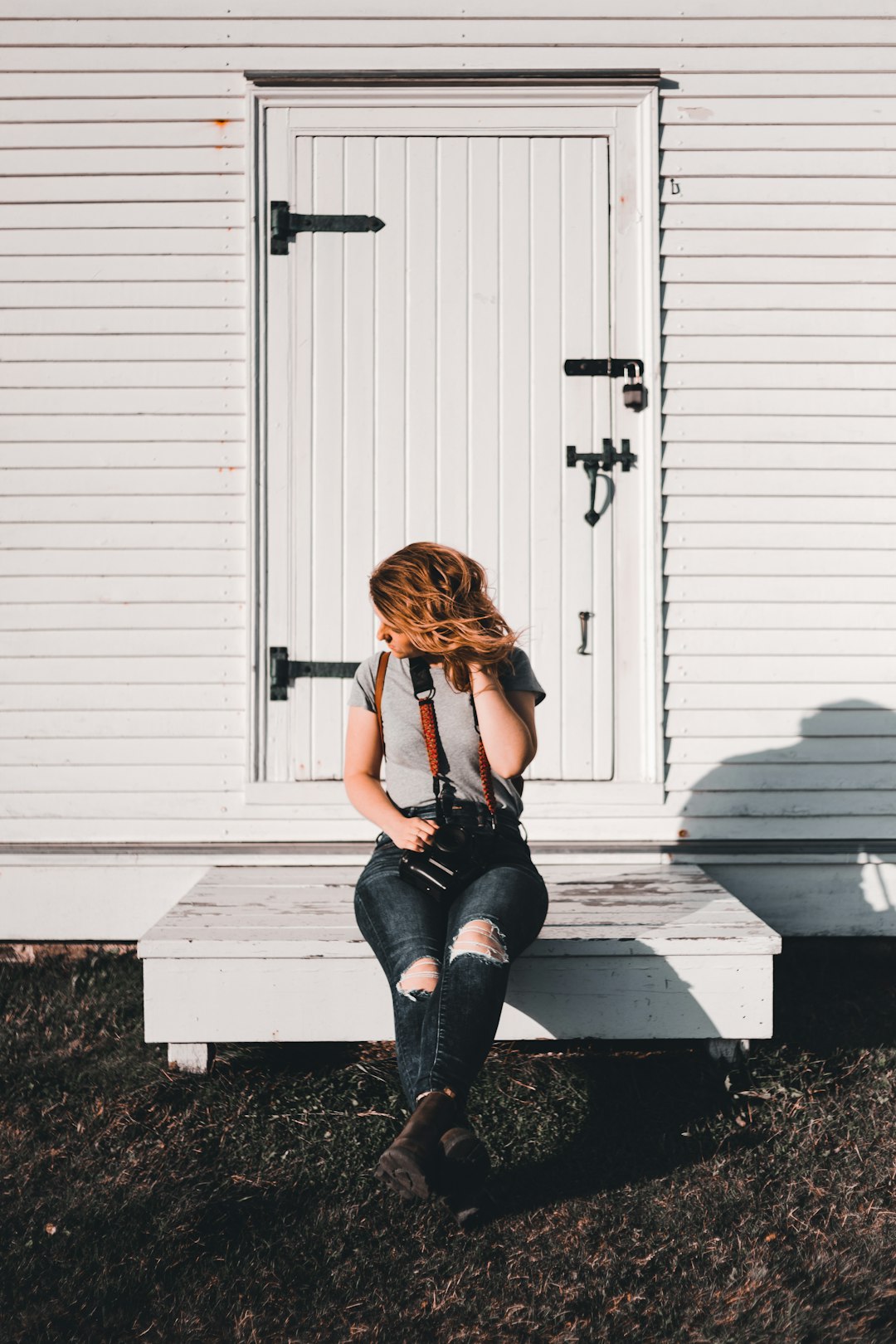 woman in black tank top and blue denim jeans sitting on white wooden wall during daytime