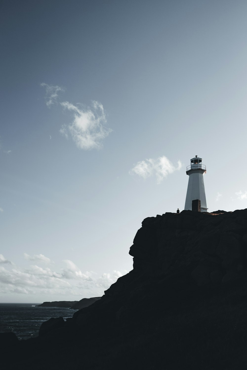 white lighthouse on black rock formation under blue sky during daytime