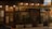 A quaint cafe facade featuring wooden paneling and vintage signs that read 'Cafe Riche.' Warm glowing lights illuminate the exterior, and potted plants add a touch of greenery. The entrance is adorned with glass doors and windows showcasing various posters and notices.