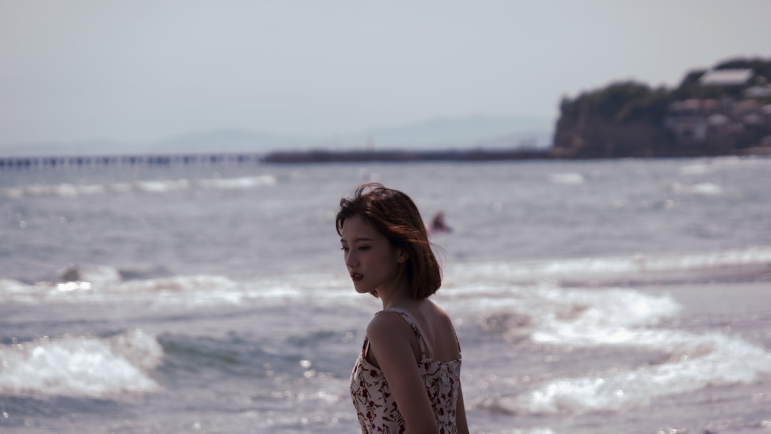 woman in white and black floral tank top standing on seashore during daytime