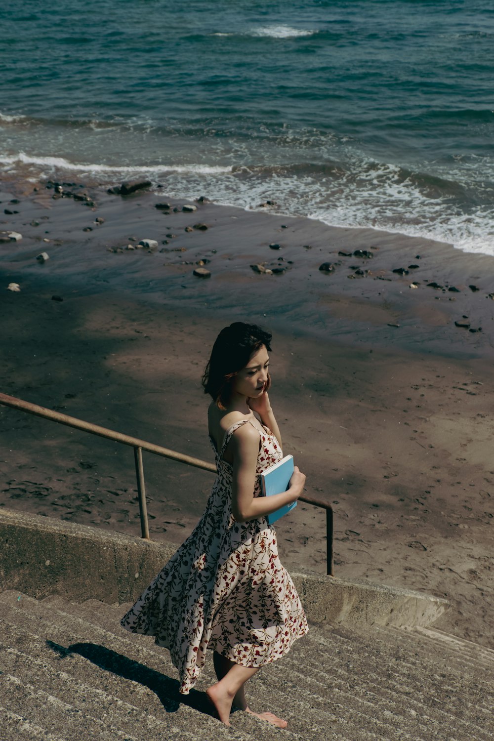 낮 동안 해변에 서 있는 흑백 꽃무늬 스파게티 스트랩 드레스를 입은 여자
