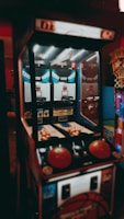 An indoor basketball arcade game with a retro design, featuring two hoops, multiple basketballs, and score displays. The game is illuminated by overhead lights, casting a vintage ambiance.