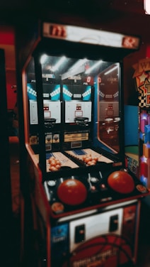 An indoor basketball arcade game with a retro design, featuring two hoops, multiple basketballs, and score displays. The game is illuminated by overhead lights, casting a vintage ambiance.