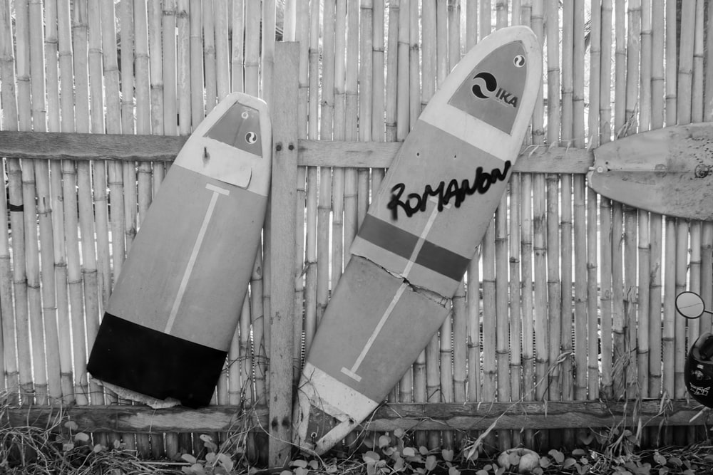 grayscale photo of two surfboard on wooden fence