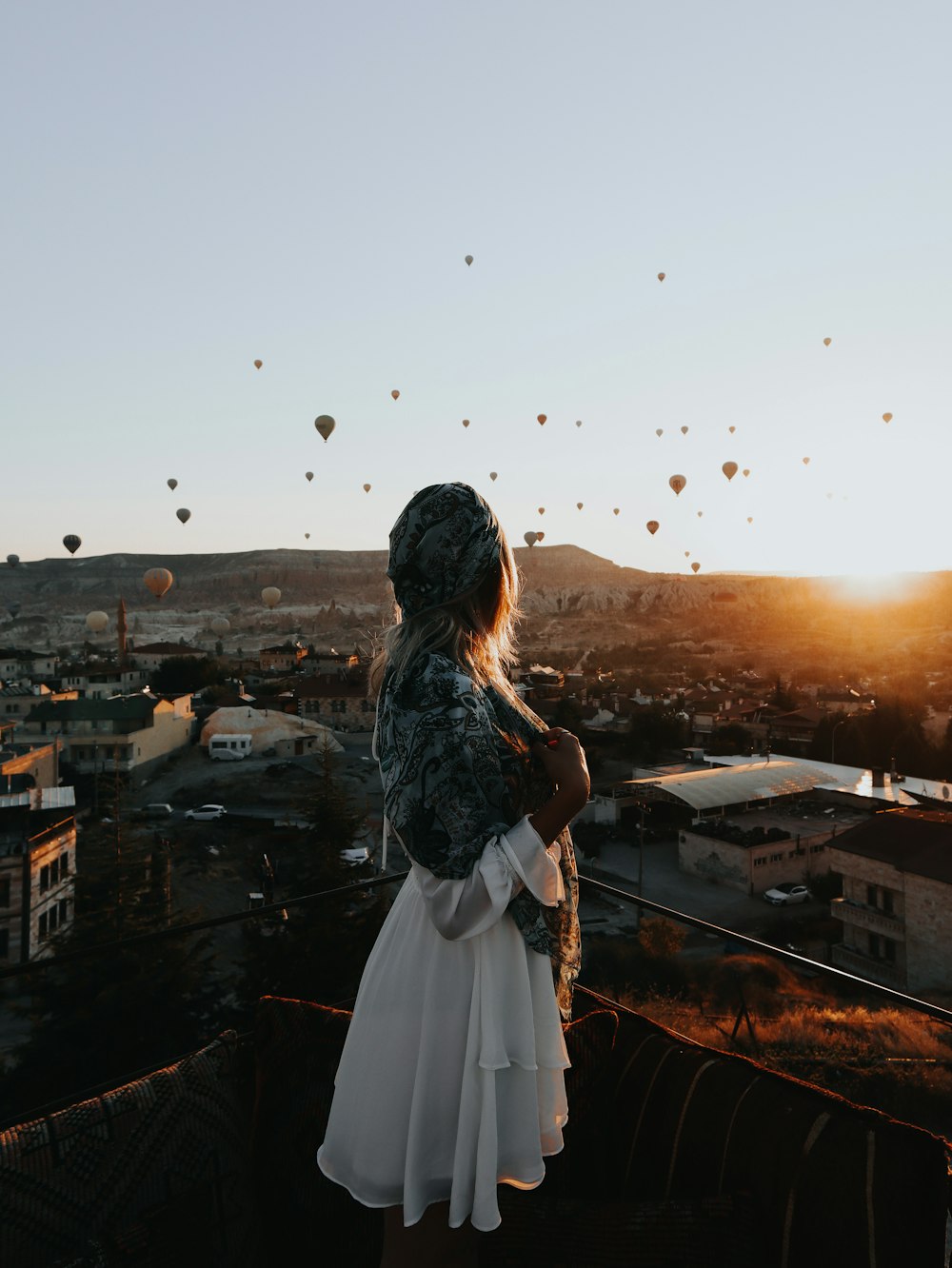 Frau in weißem Kleid, die bei Sonnenuntergang auf dem Dach des Gebäudes steht