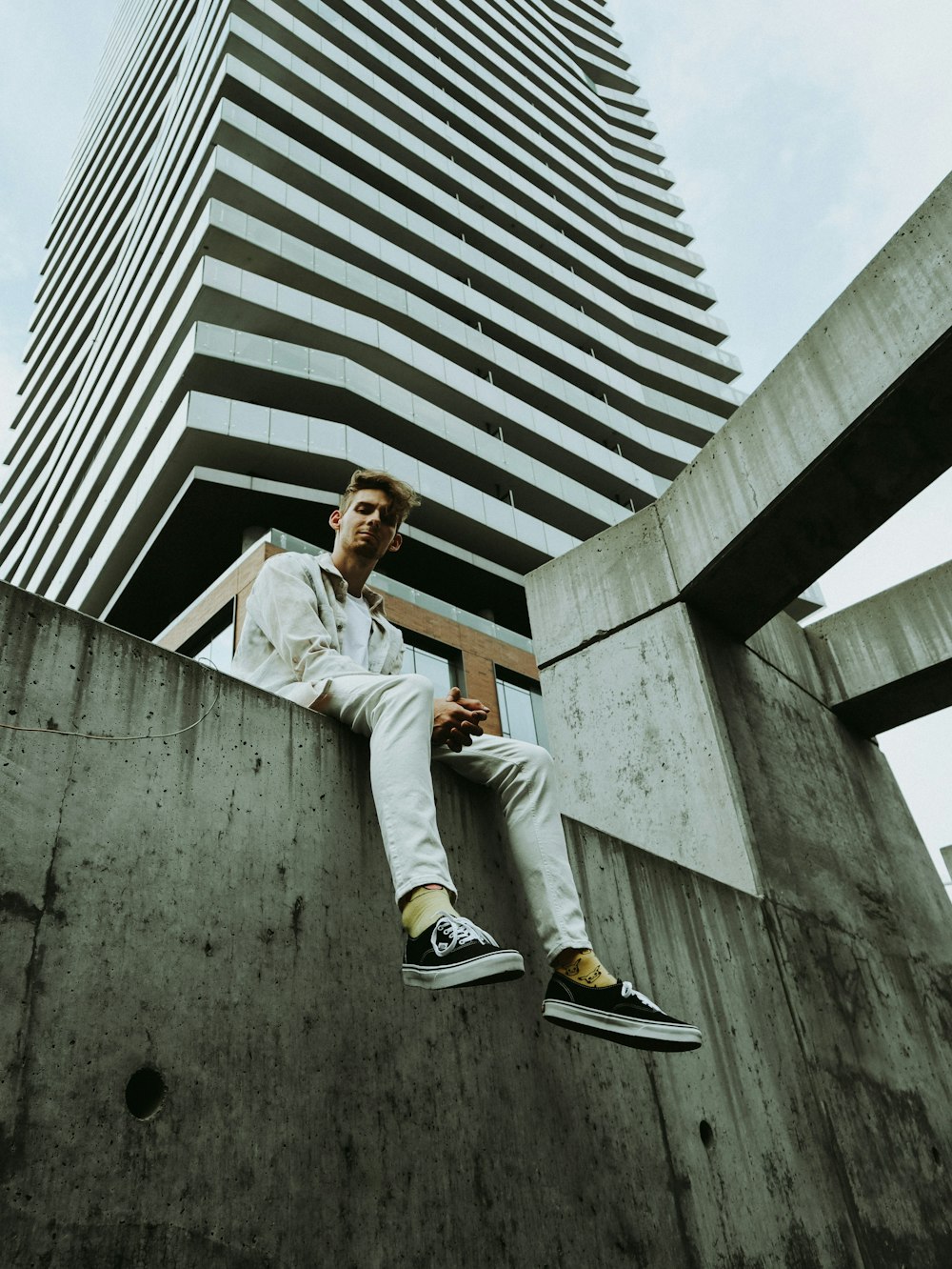 man in white dress shirt and brown pants sitting on gray concrete wall during daytime