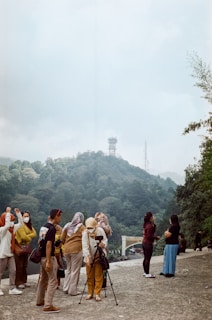 Smiling tourists taking photos in front of a lush mountain landscape during a Jendela Tours excursion.