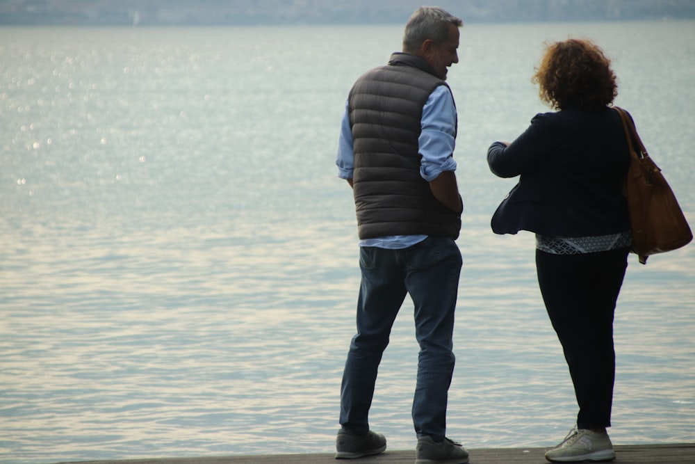 man in black and gray striped long sleeve shirt and blue denim jeans standing on beach