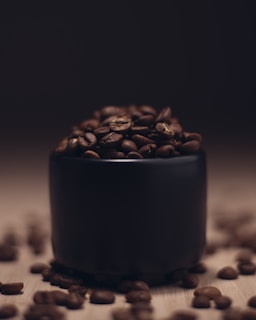 brown coffee beans in black ceramic mug by Mokaa