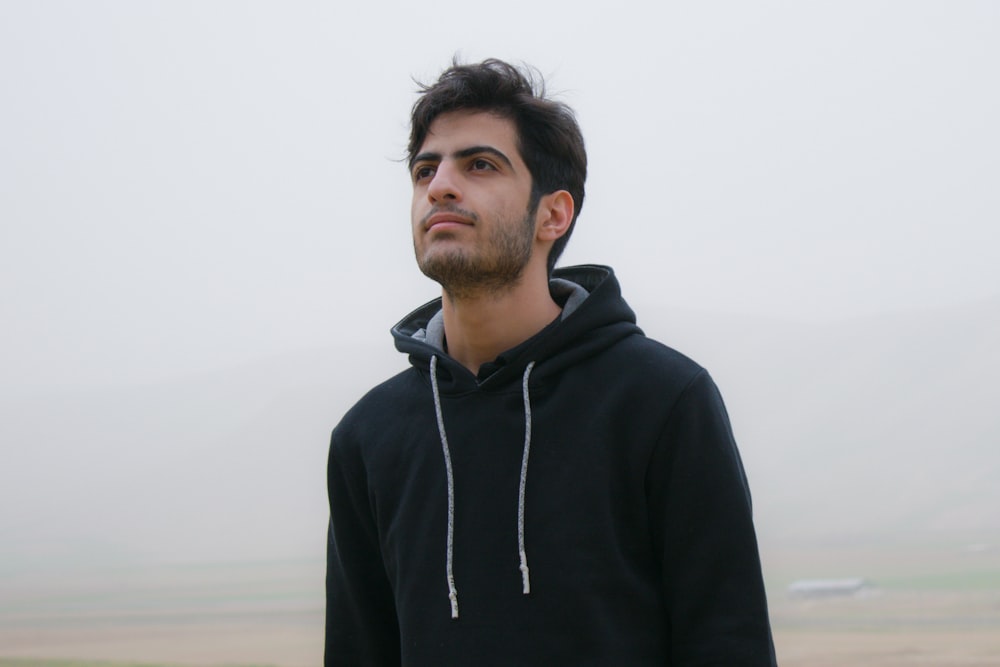 a man in a black hoodie standing in a foggy field