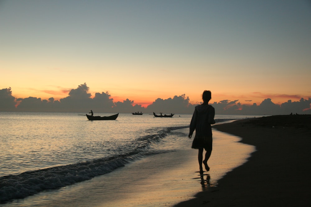 a person walking on a beach at sunset