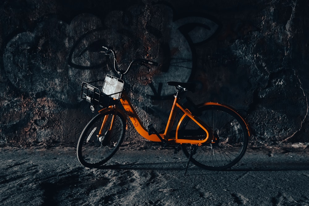an orange bicycle parked in front of a rock wall