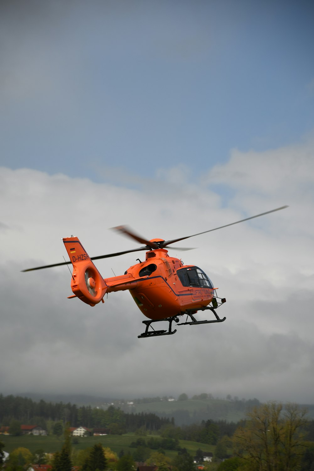 an orange helicopter flying through a cloudy sky