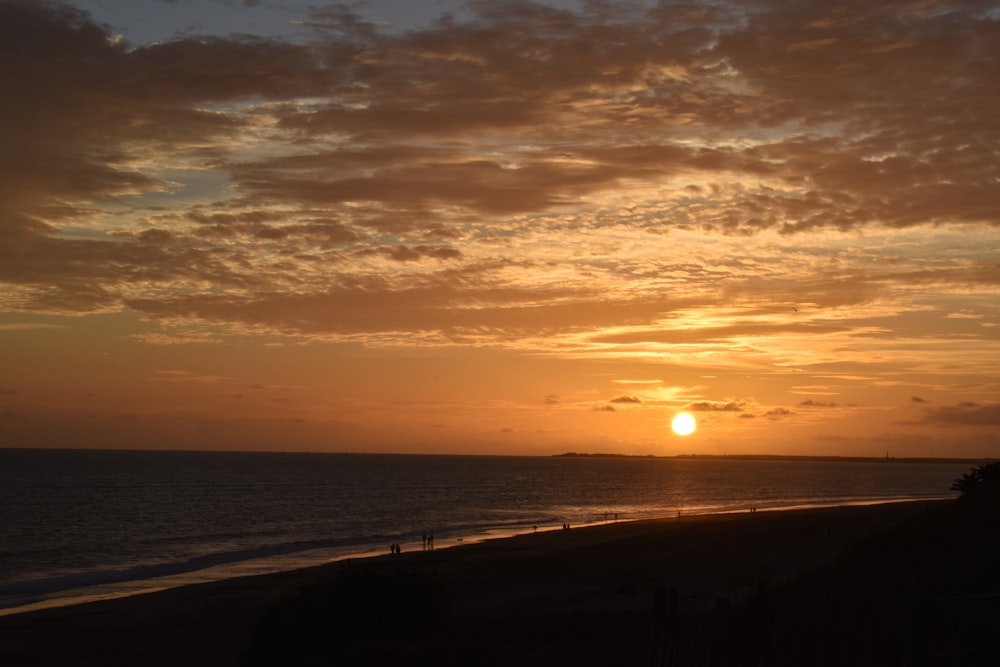 the sun is setting over the ocean on a cloudy day