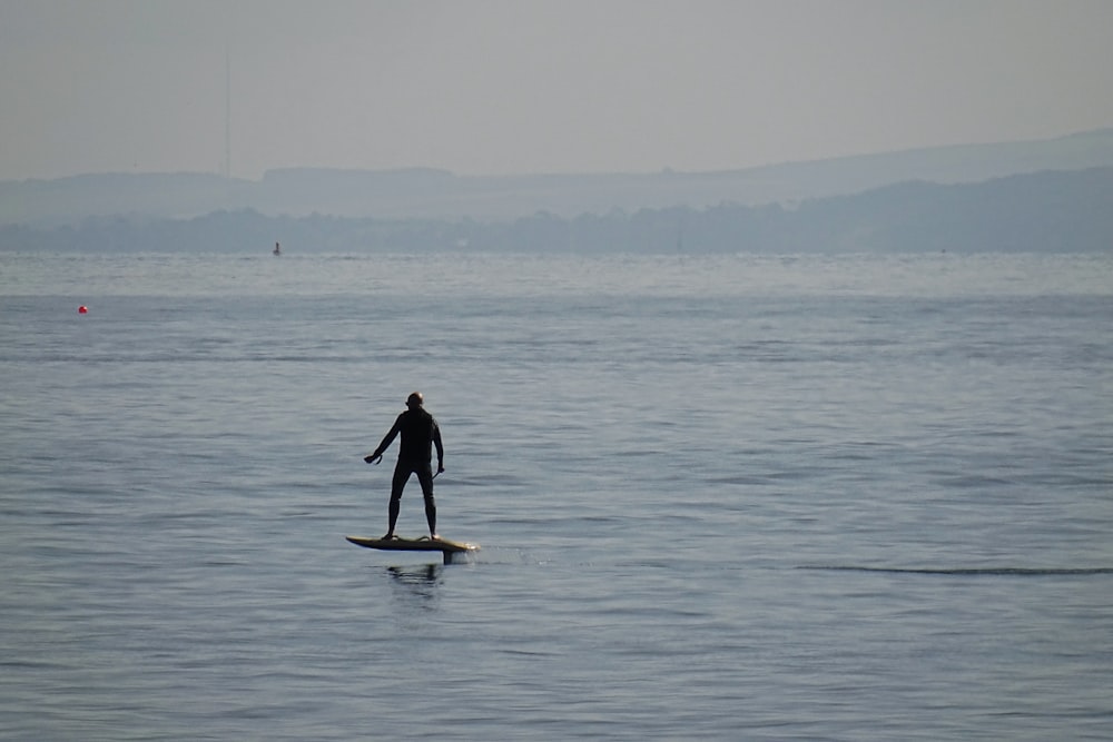 昼間、海に浮かぶ白いサーフボードの上に立つ黒いウェットスーツを着た男